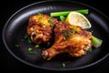 Close-up of a spicy fried chicken drumstick with green onions and lemon wedges on a black plate