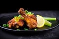 Close-up of a spicy fried chicken drumstick with green onions and lemon wedges on a black plate