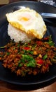 Close up spicy stir fried minced beef with basil and fried egg on white rice in Thai style on black dish or plate Royalty Free Stock Photo