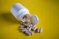 Close up of spilled medical pills from pill bottle on yellow background Royalty Free Stock Photo