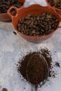 Spoonful of coffee and clay pots of roasted coffee beans on white marble surface