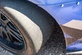 Close-up of a sports car wheel with a worn out slick tire and a blue bumper in the sun. Horizontal orientation. High