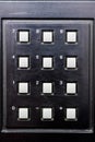 Close-up of square buttons on a black plastic panel, buttons from 0 to 9 and signs + and -