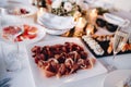 Close-up of a square white plate with prosciutto on a festively served table with sushi set and tomatoes on a white