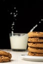 Close-up of stack of chocolate cookies and glass of milk, selective focus, on white wooden table, black background, vertical, Royalty Free Stock Photo