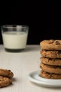 Close-up of stack of chocolate cookies and glass of milk, selective focus, on white wooden table, black background, vertical, Royalty Free Stock Photo