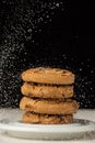 Close-up of stack of chocolate cookies on plate, with falling sugar, on white wooden table, black background, in vertical Royalty Free Stock Photo