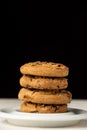 Close-up of stack of chocolate cookies on plate, on white wooden table, black background Royalty Free Stock Photo