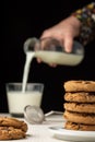 Close-up of stack of chocolate cookies and woman`s hand pouring milk into a glass, selective focus, on white wooden table, Royalty Free Stock Photo