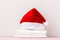 Close-up of a stack of clean white bedding and a Santa hat, on a table against a light wall. Copy space