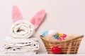 A close-up of a stack of clean white bedding, towels and Easter bunny ears, a basket of eggs on a table.