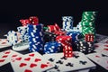 Close up stack of different colored poker chips, playing cards and dices isolated over black casino table background