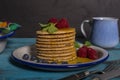 Close-up of a stack of Dutch waffles with raspberries, blueberries and honey on blue wooden background. Isolated image