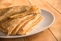 Close up on a stack of folded crepes french pancakes on a plate, wood background