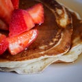 Close up of a stack of homemade pancakes on a white plate with cut strawberries and maple syrup on top.