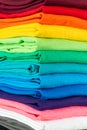 Close-up stack of many fresh fabric cotton t-shirts in colorful rainbow colors. Pile of various colored shirts background