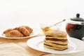 Close up of a stack of sweet tasty pancakes, croissants, honey in a bowl with dipper and a teapot, Breakfast served on