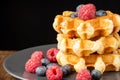 Close-up of stacked waffles with raspberries and blueberries on dark plate, on wooden table, black background, Royalty Free Stock Photo