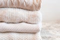 Close up of stacked wool knitted sweaters or jumpers, in white and light tones, cozy image, soft fabrics in white background