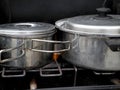 Close up of stainless steel sauce pans on a camp stove with flames licking their sides