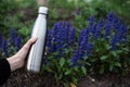 Close-up of stainless thermos bottle for water in field of sage flower.