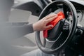 Close up of steering wheel inside of car and mans hand with cloth. Cleaning auto interior. Automobile detailing service