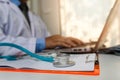 Close-up of stethoscope is lying on the clipboard near a doctor typing on laptop computer Royalty Free Stock Photo