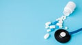 Close up stethoscope and pills spilling out of pill bottle on blue background. Medicine, medical insurance or pharmacy concept Royalty Free Stock Photo