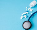 Close up stethoscope and pills spilling out of pill bottle on blue background. Medicine, medical insurance or pharmacy Royalty Free Stock Photo