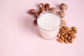 Close-up of a glass of healthy organic raw vegan plant based milk and assortment of nuts on pink background. Copy space
