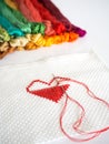 Stitching red heart shape on white fabric on white background.