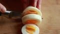A close-up stock video capturing the hands of a woman delicately slicing a boiled egg on a wooden cutting board