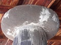 Close up of a stone pillar on a rustic wooden roof with beams to support loads. Granite column and dark wood ceiling detail.