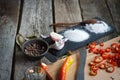 Close-up of stone stand with heaps of salt, sugar, garlic, allspice, bay leaf next to a board with chopped chili peppers on an old