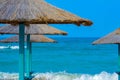 Close-up of straw beach umbrellas providing shade near the wavy water of the Black Sea on sandy shoreline on a sunny clear summer