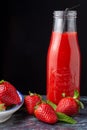 Close-up of strawberries on plate, glass bottle with strawberry juice and black straw on blue marble and black background, vertica Royalty Free Stock Photo