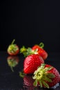 Close-up of strawberries on wet black slate stone and reflection, with selective focus, black background, vertical,