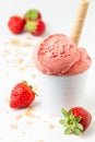 Close up of strawberry ice cream in white bowl on white table with two strawberries, wafers and crumbles Royalty Free Stock Photo