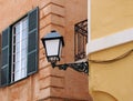 Street corner view of an ornate old street lamp mounted on a painted yellow house with iron balcony and window with open Royalty Free Stock Photo