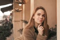 Close-up street portrait of a young girl wearing a coat, on the background of a beige wall, looks up and thinks. Street photo of a