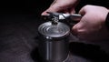 Hands with tin-opener make an incision on lid in metal tin can on black table