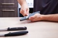 Strong male hands sharpen a kitchen metal knife with a grindstone. Home household knife sharpening Royalty Free Stock Photo