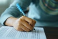 Close up of student`s hand holds a pen write on answer sheet. Student answers multiple choice questions on wooden table in examin