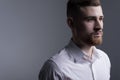 Close-up, studio dramatic portrait of a handsome bearded guy in a white shirt. On a gray background