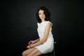 Close up studio portrait of beautiful young woman with evening make-up in white short dress sitting on the bar chair Royalty Free Stock Photo