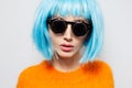 Close-up studio portrait of fashionable pretty girl with blue hair, wearing round sunglasses and orange shirt on white background. Royalty Free Stock Photo