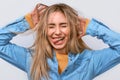 Close up studio portrait of funny young blonde woman with hands in the hair dressed casual blue shirt, making funny faces Royalty Free Stock Photo