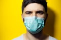 Close-up studio portrait of young man wearing medical flu mask on background of yellow color. Royalty Free Stock Photo