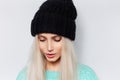 Close-up studio portrait of young pretty girl with blonde hair wearing black hat and blue sweater on white background. Royalty Free Stock Photo