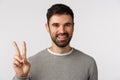 Close-up studio shot cheerful, handsome bearded male in grey sweater, show peace sign and smiling carefree, stay upbeat